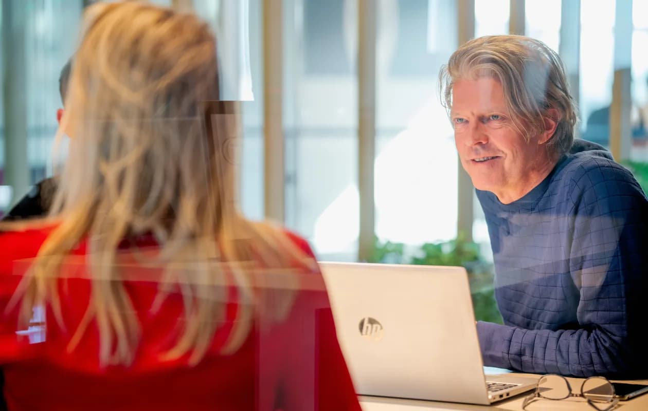 Persoon kijkt lachend tijdens een meeting met een laptop voor zich