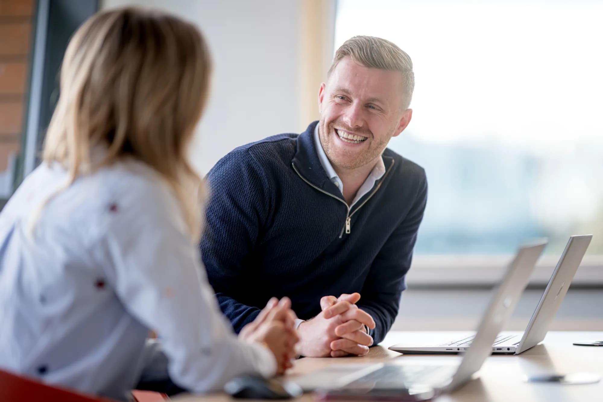 Twee personen voeren een gesprek op kantoor met laptops voor zich
