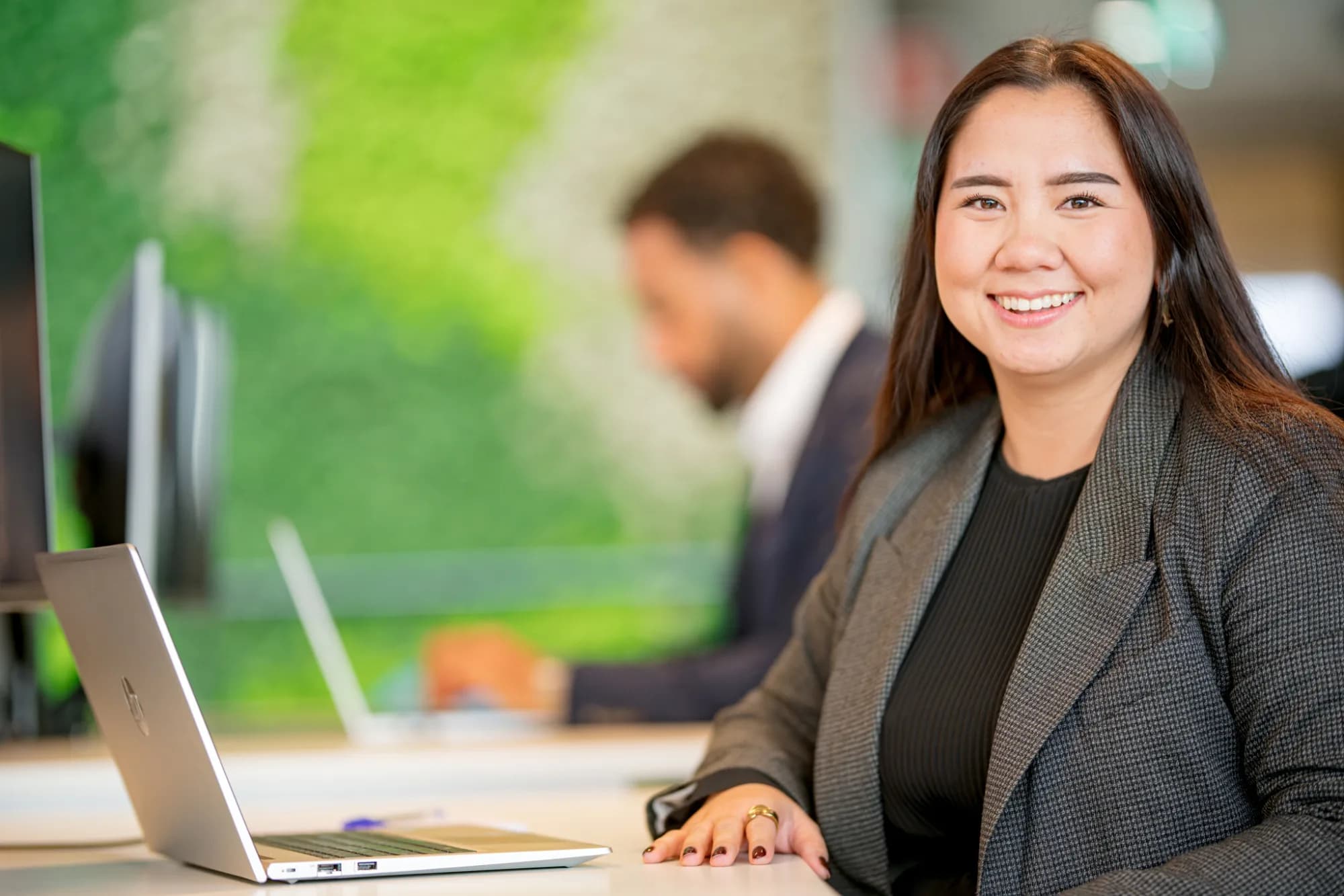 Woman smiles behind her laptop at the office