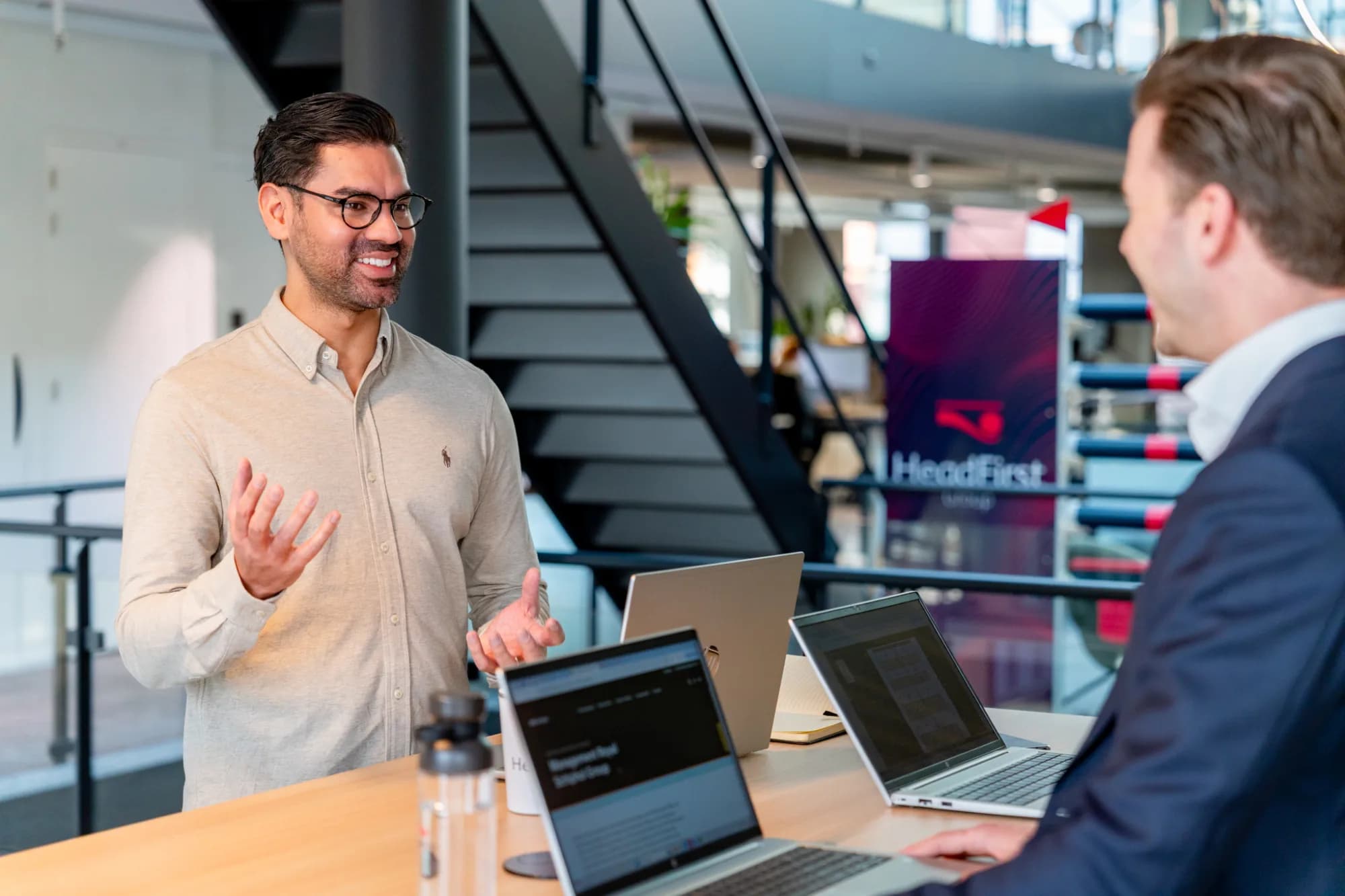 een man legt iets uit aan een andere mannelijke collega aan bureau op kantoor