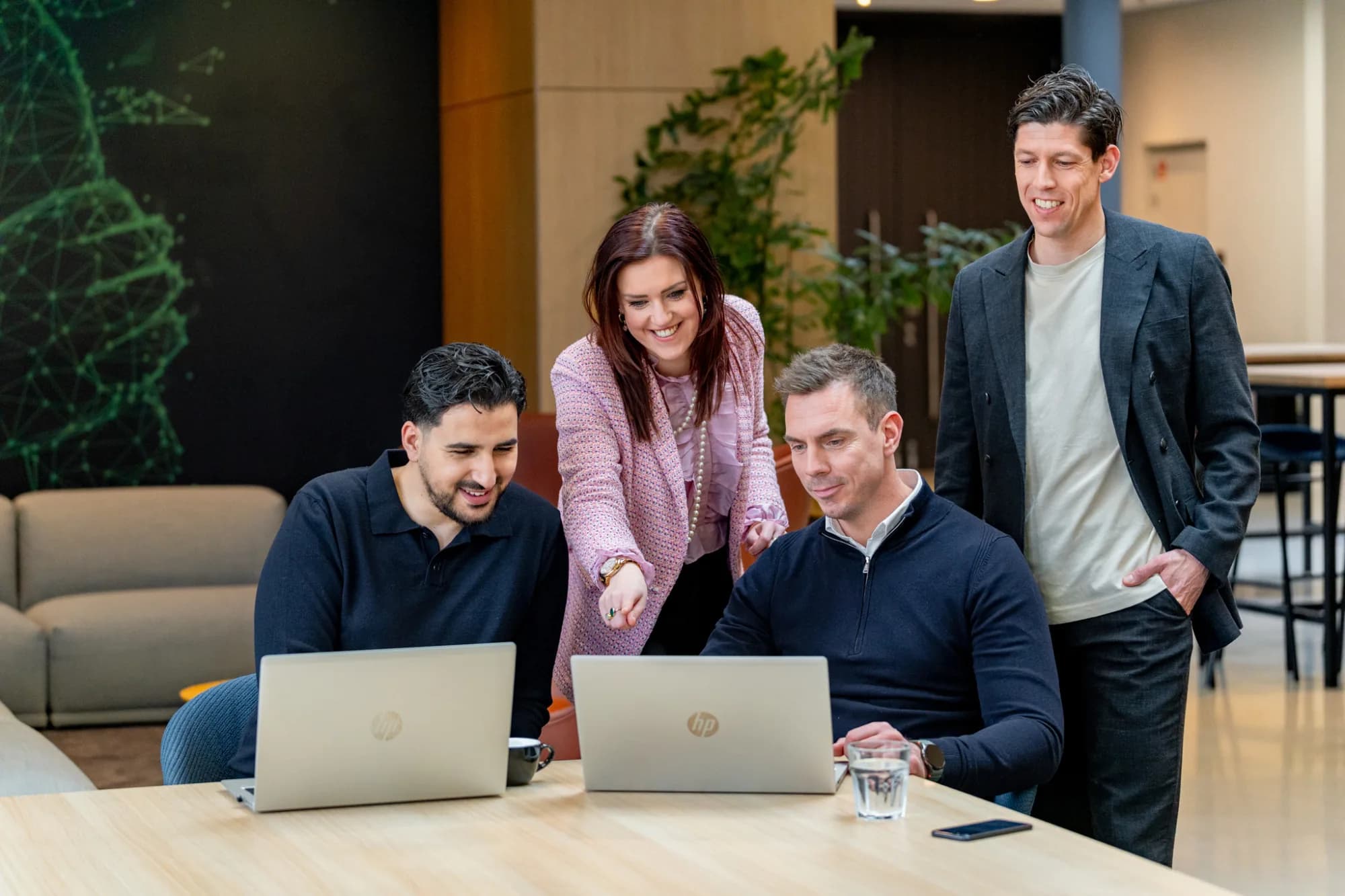 4 collega's met 2 laptops kijkend naar een scherm in het bedrijfsrestaurant