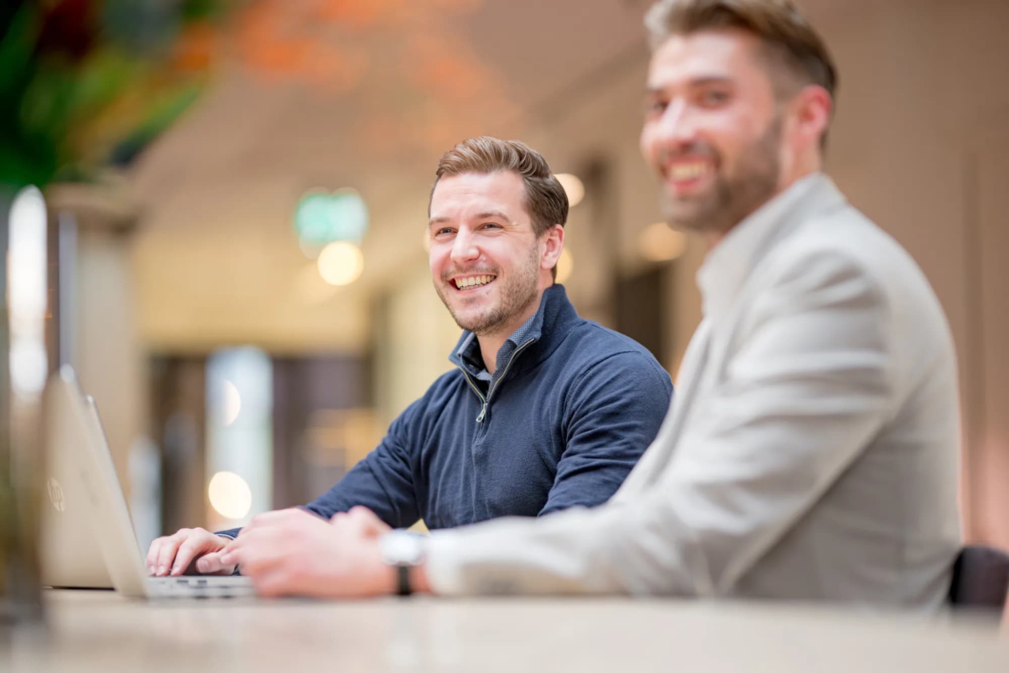 Twee collega’s lachen tijdens meeting op kantoor, over hoe HeadFirst maatschappelijke impact en inclusie in het inhuurproces verwerkt.